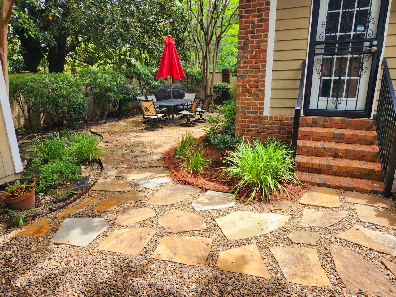 Stone patio and walkway beside brick steps and landscaped beds