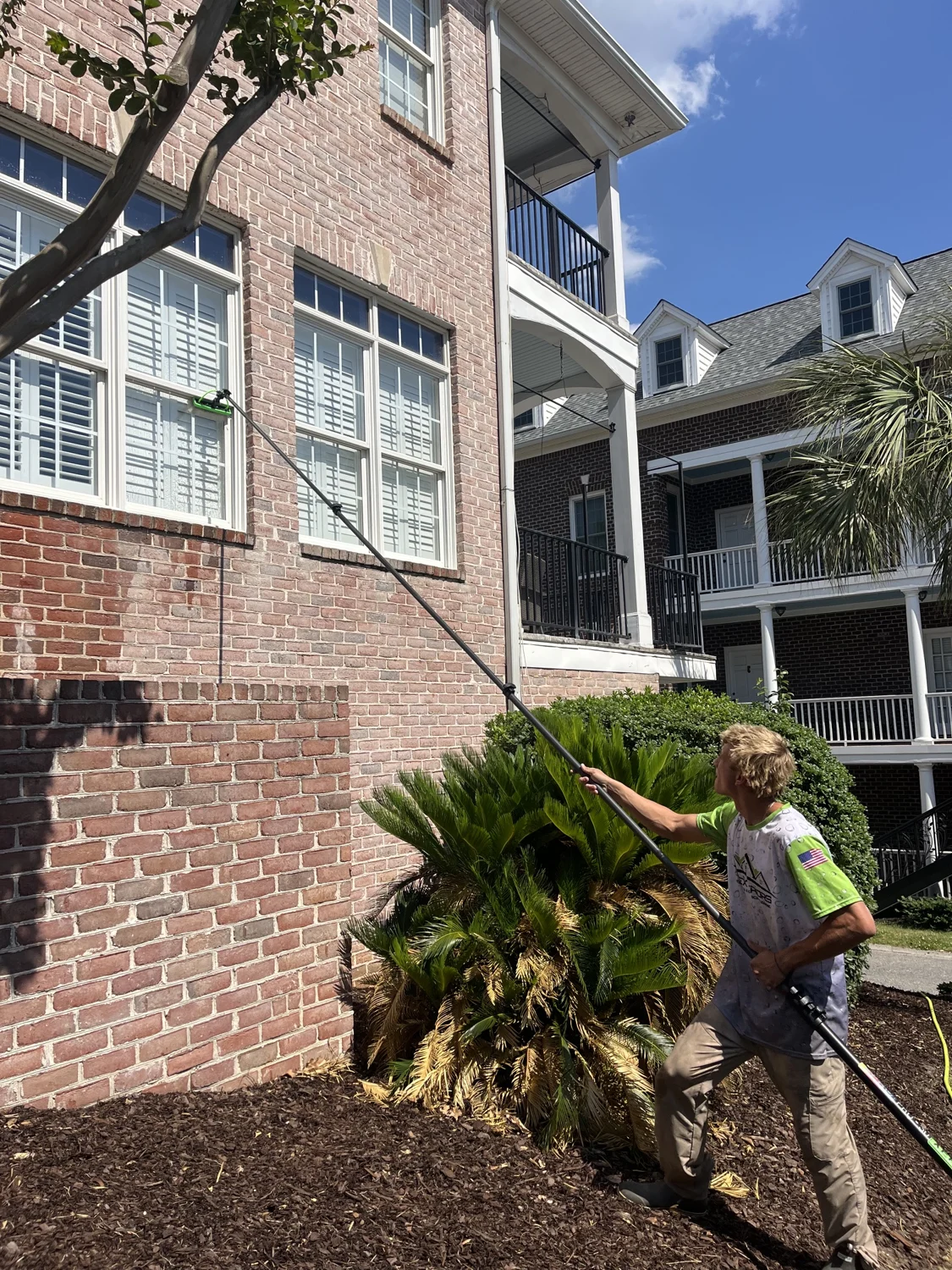 Andrew cleaning tall exterior windows on a brick home with a water-fed pole